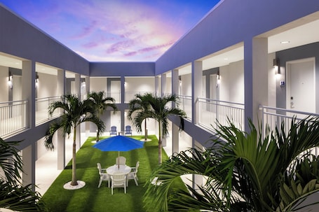 A hotel atrium with a central lawn, palm trees, and a blue umbrella.