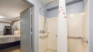 Un baño con ducha, barras de apoyo y un inodoro.