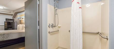 A bathroom with a shower, grab bars, and a toilet.