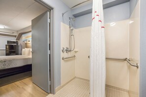 Un baño con ducha, barras de apoyo y un inodoro.