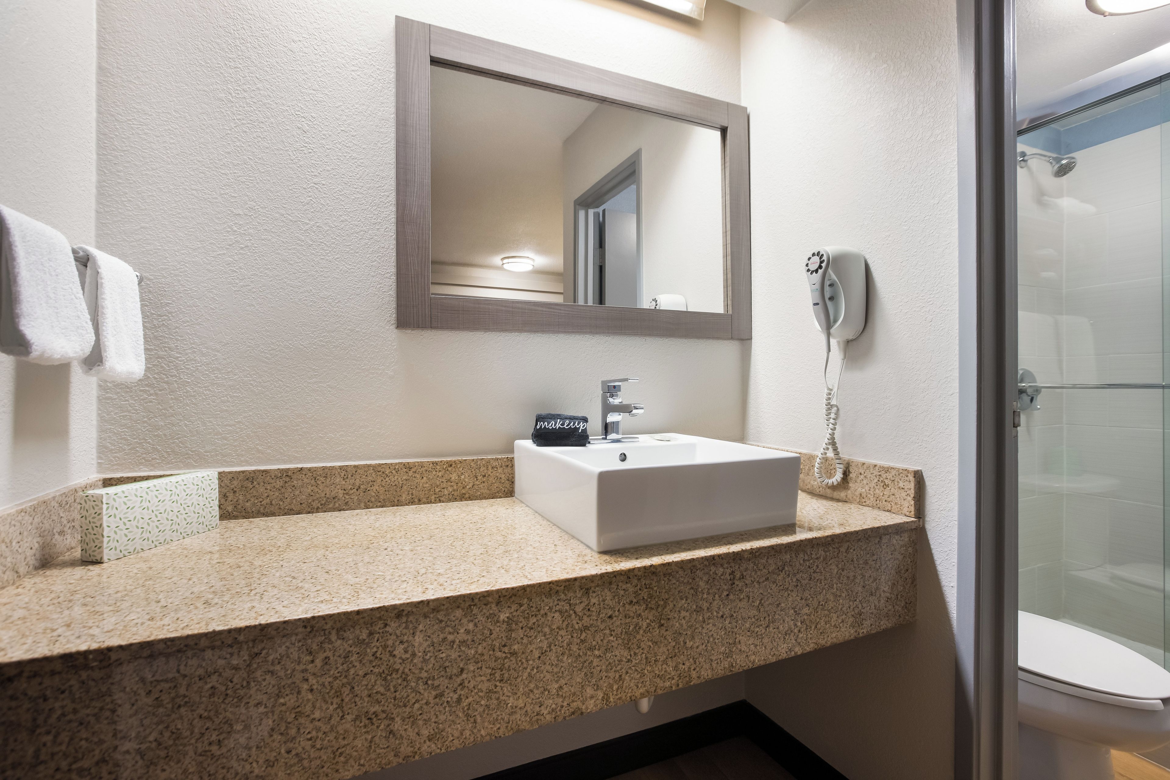 A bathroom with a sink, mirror, towel rack, and a shower area.