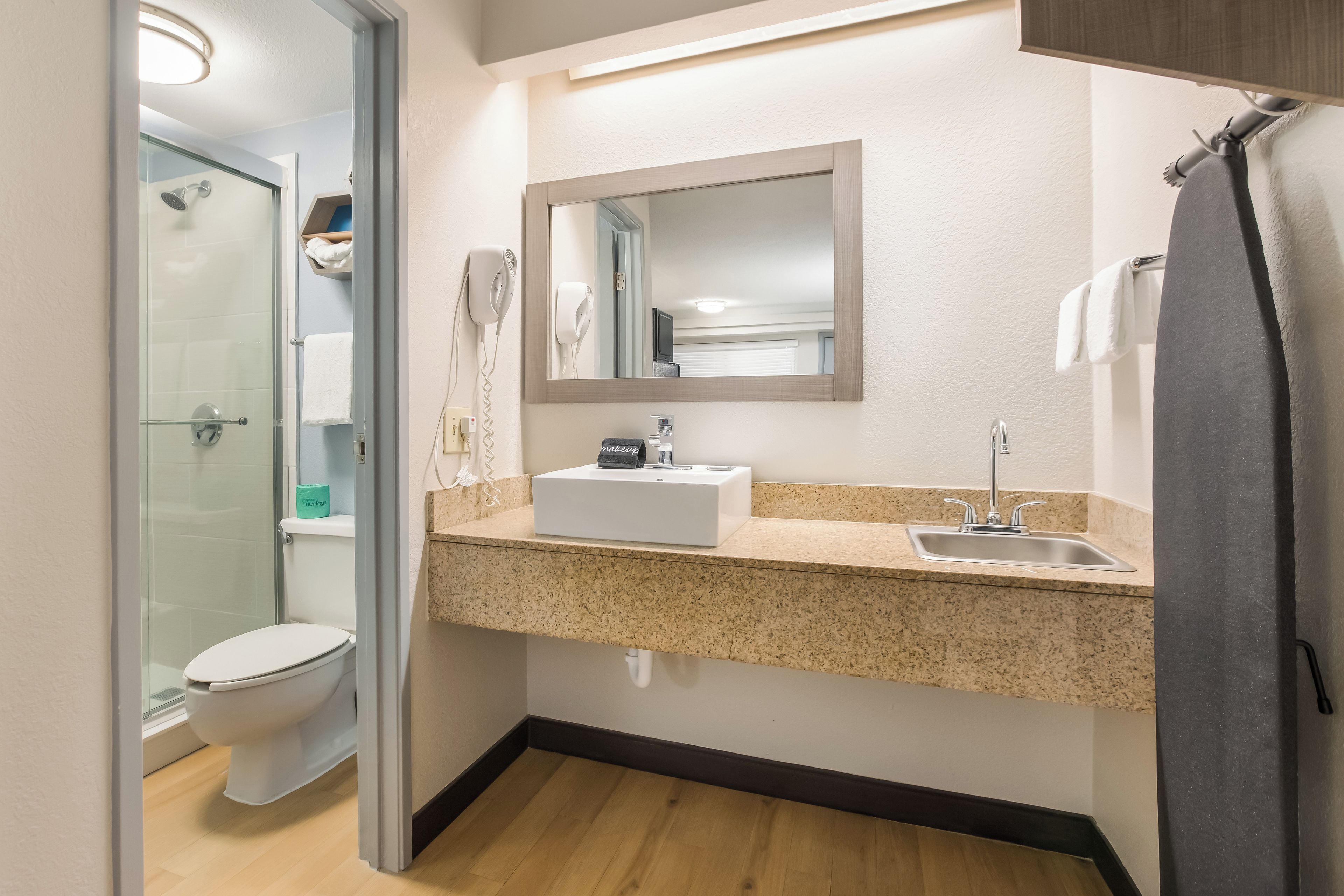 Un baño moderno con cabina de ducha de vidrio, inodoro blanco, lavabo con espejo y una toalla colgada en la pared.