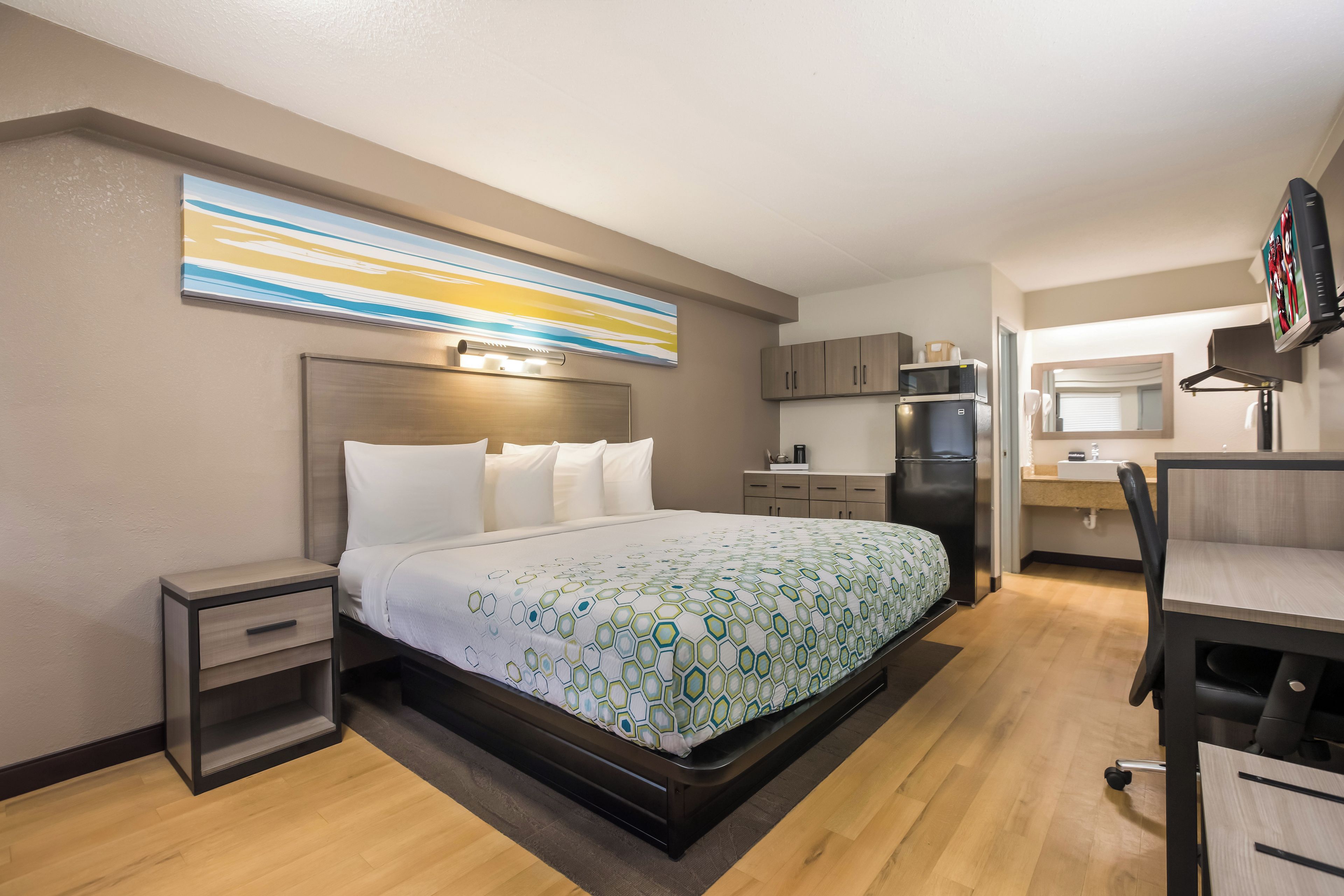 A hotel room with a bed, bedside tables, a desk, a refrigerator, and a television.