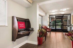 Habitación de hotel con escritorio, impresora, señal roja que indica Wi-Fi gratuito, una silla roja y una planta en maceta.