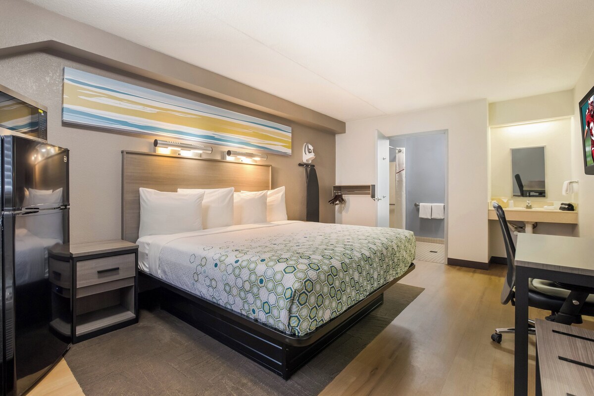 Una habitación de hotel con cama, escritorio, refrigerador y baño.