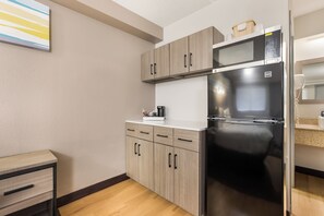 Cocina compacta con refrigerador negro, armarios de madera y una encimera con cafetera.