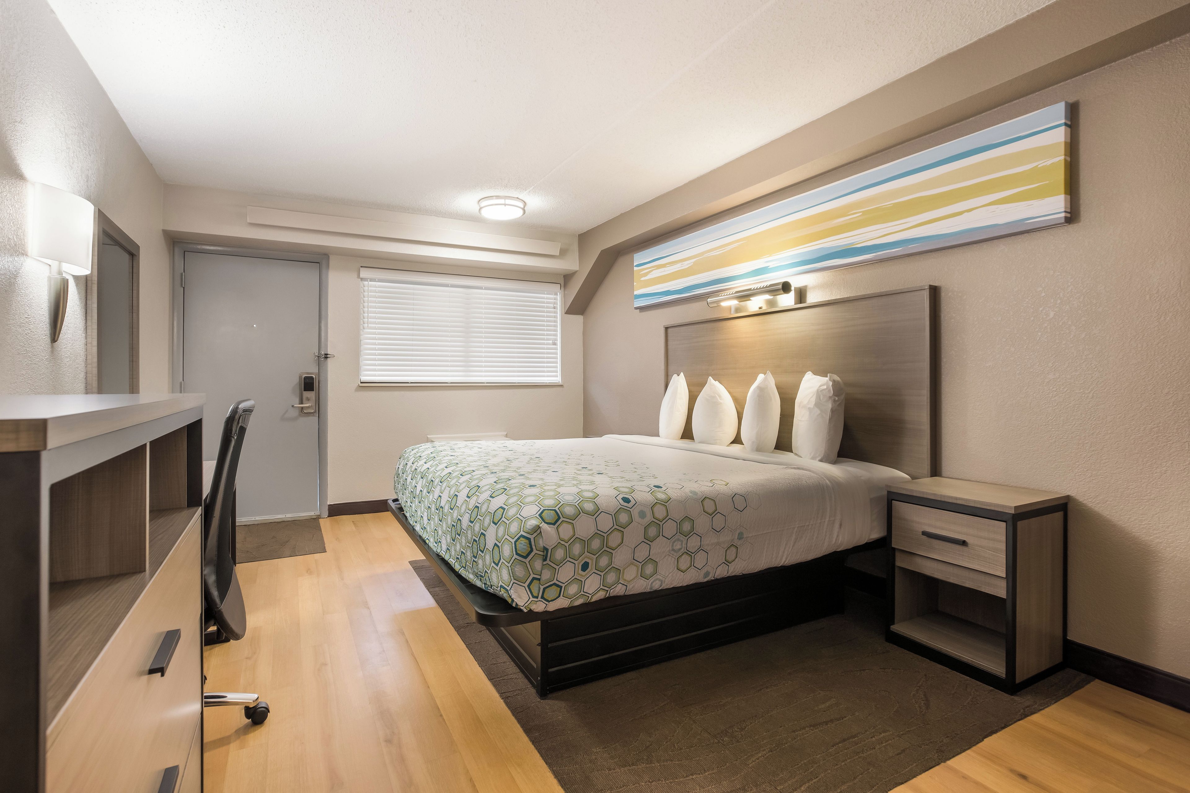 Ein Hotelzimmer mit Bett, Nachttisch, Schreibtisch, Stuhl und einem Fenster mit Jalousien.