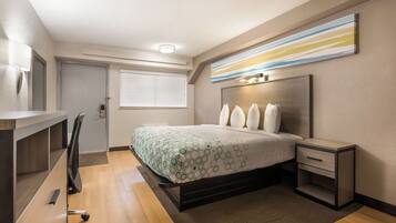 Ein Hotelzimmer mit Bett, Nachttisch, Schreibtisch, Stuhl und einem Fenster mit Jalousien.