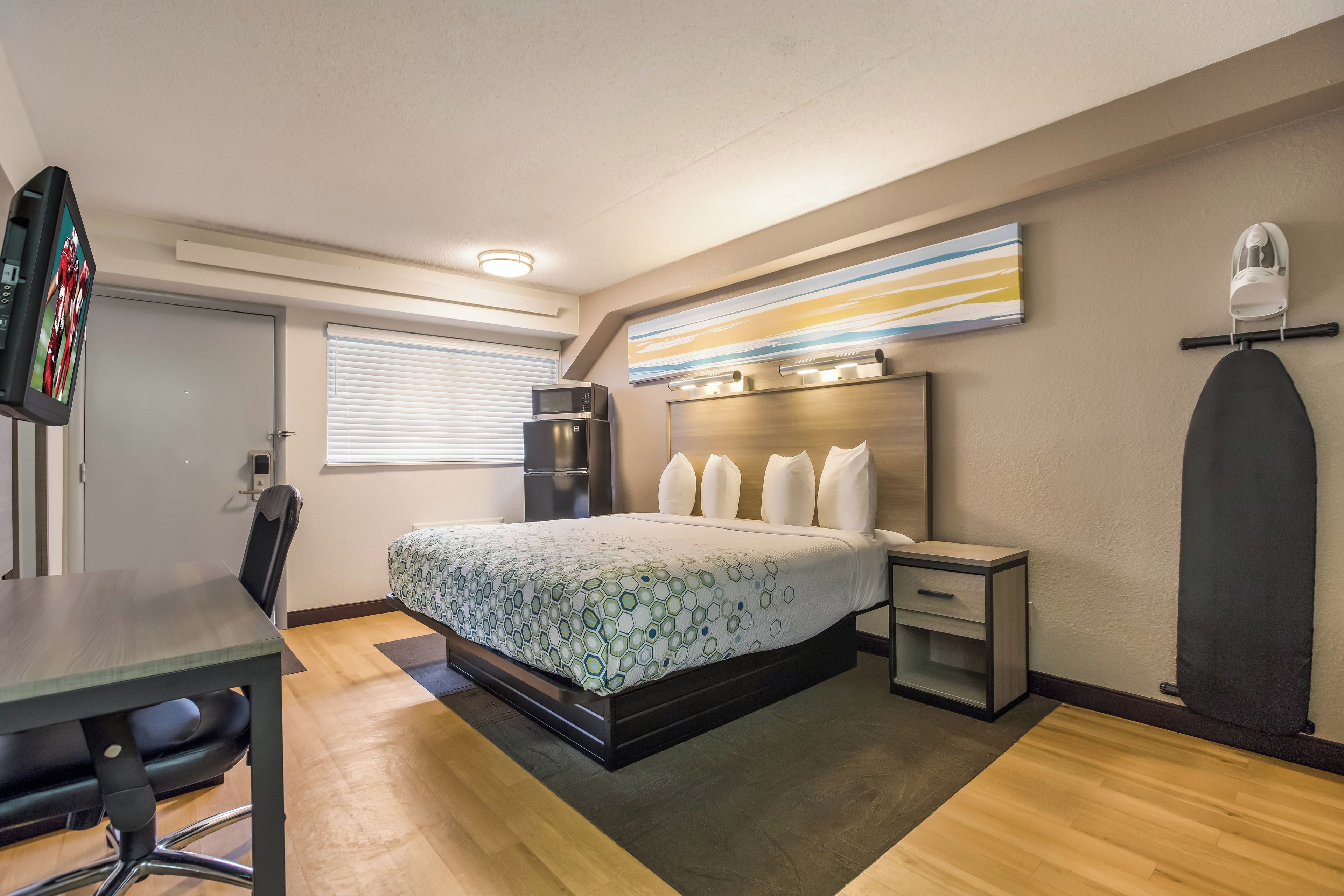Ein Hotelzimmer mit Bett, Nachttisch, Sessel, Schreibtisch und einer Mikrowelle.
