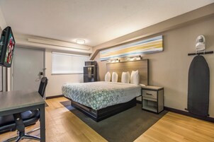 Habitación de hotel con cama, mesita de noche, silla, escritorio y microondas.