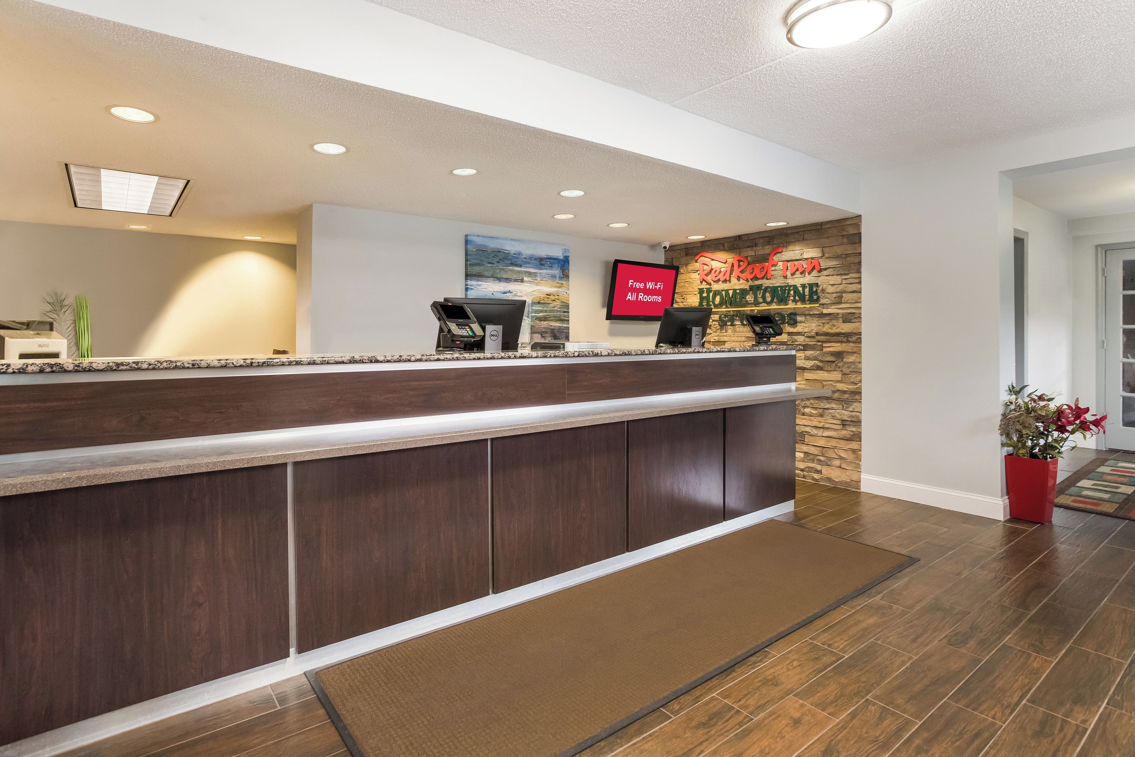 A hotel reception desk with a digital screen, a flat-screen TV, and a sign indicating free Wi-Fi in all rooms.