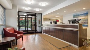 Un área de recepción con piso de madera, una silla roja, un escritorio, una computadora y vista al exterior a través de puertas de vidrio.