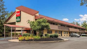 A motel with a red roof, a covered parking area, and a landscaped front yard.