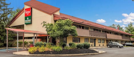 A motel with a red roof, a covered parking area, and a landscaped front yard.