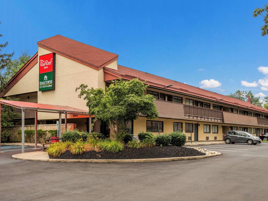 A motel with a red roof, a covered parking area, and a landscaped front yard.