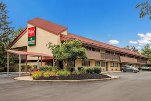 Un motel con techo rojo, estacionamiento techado y jardín delantero ajardinado.