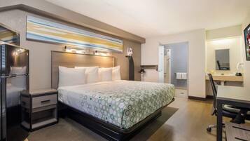Quarto de hotel com cama, escrivaninha, espelho e frigorífico.