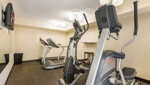 Un gimnasio con cintas de correr y máquinas elípticas, piso alfombrado y una pequeña mesa.