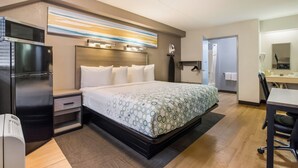 Una habitación de hotel con cama, escritorio, microondas, refrigerador y baño.
