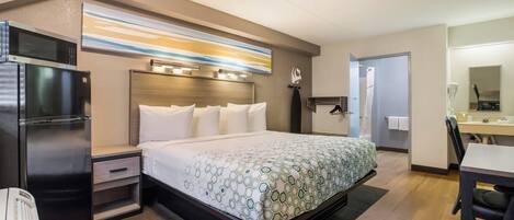 A hotel room with a bed, a desk, a microwave, a refrigerator, and a bathroom.