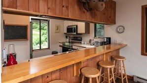 Cocina con gabinetes de madera, barra con taburetes, microondas, cafetera y vista a zonas verdes.