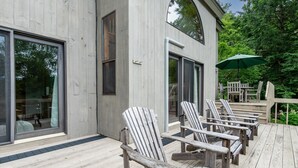 Una terraza de madera con sillas Adirondack y un paraguas verde.