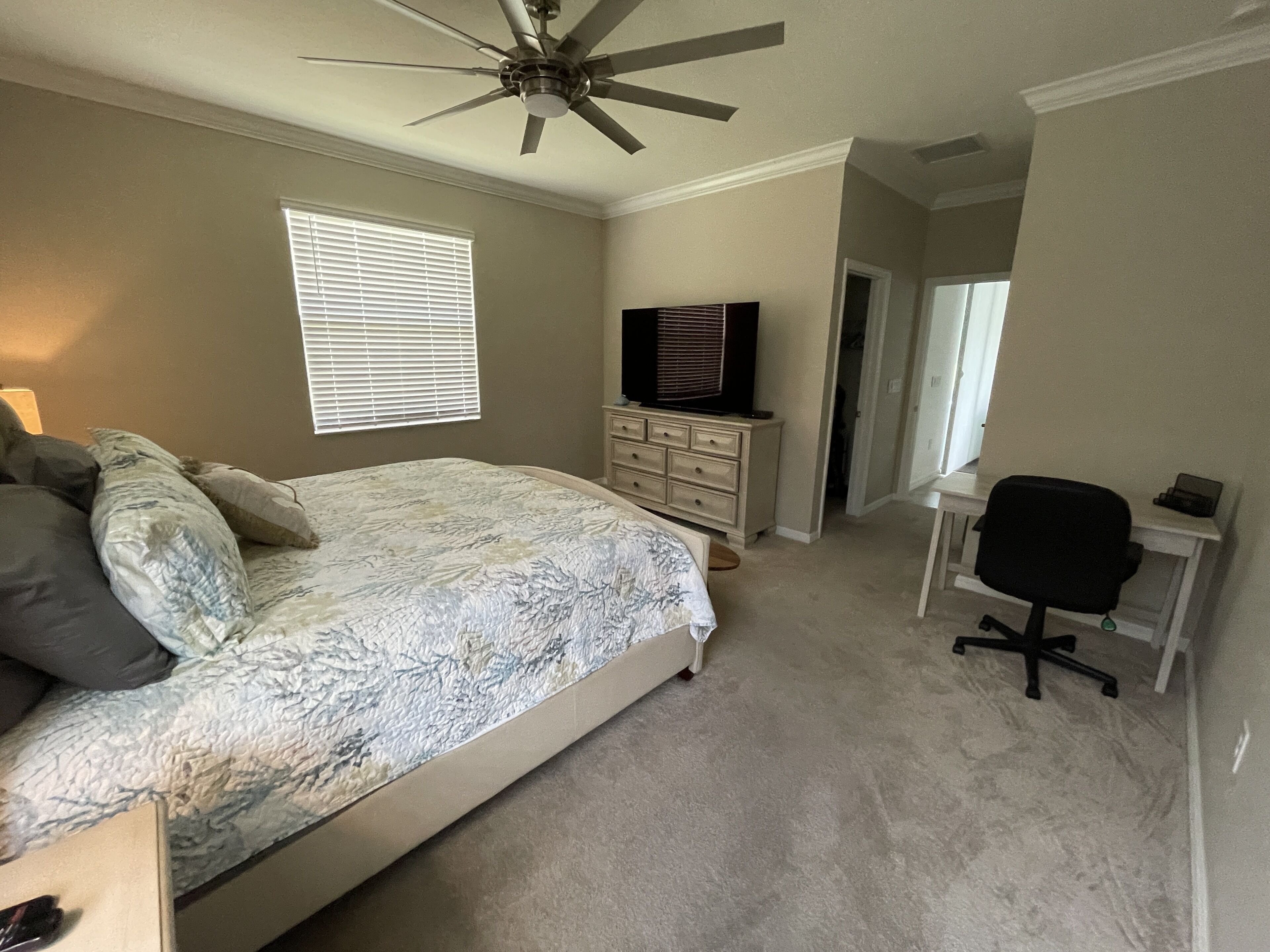 A bedroom with a bed, dresser, TV, desk, and chair.