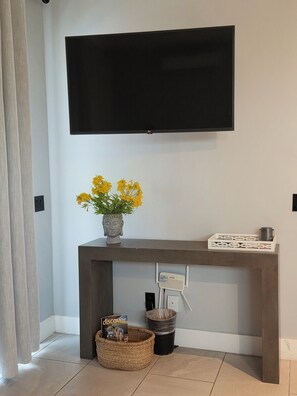 Ein modernes Wohnzimmer mit einem an der Wand befestigten Flachbildfernseher, einem Konsolentisch mit Blumenvase, einem Korb mit einem Buch und einem Mülleimer.