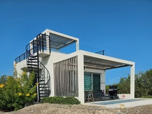 A modern two-story house with a spiral staircase, a covered outdoor seating area, and a swimming pool.