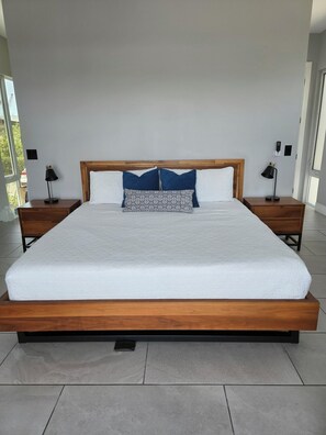 A modern bedroom with a large bed, two bedside tables, and a view of the outdoors.