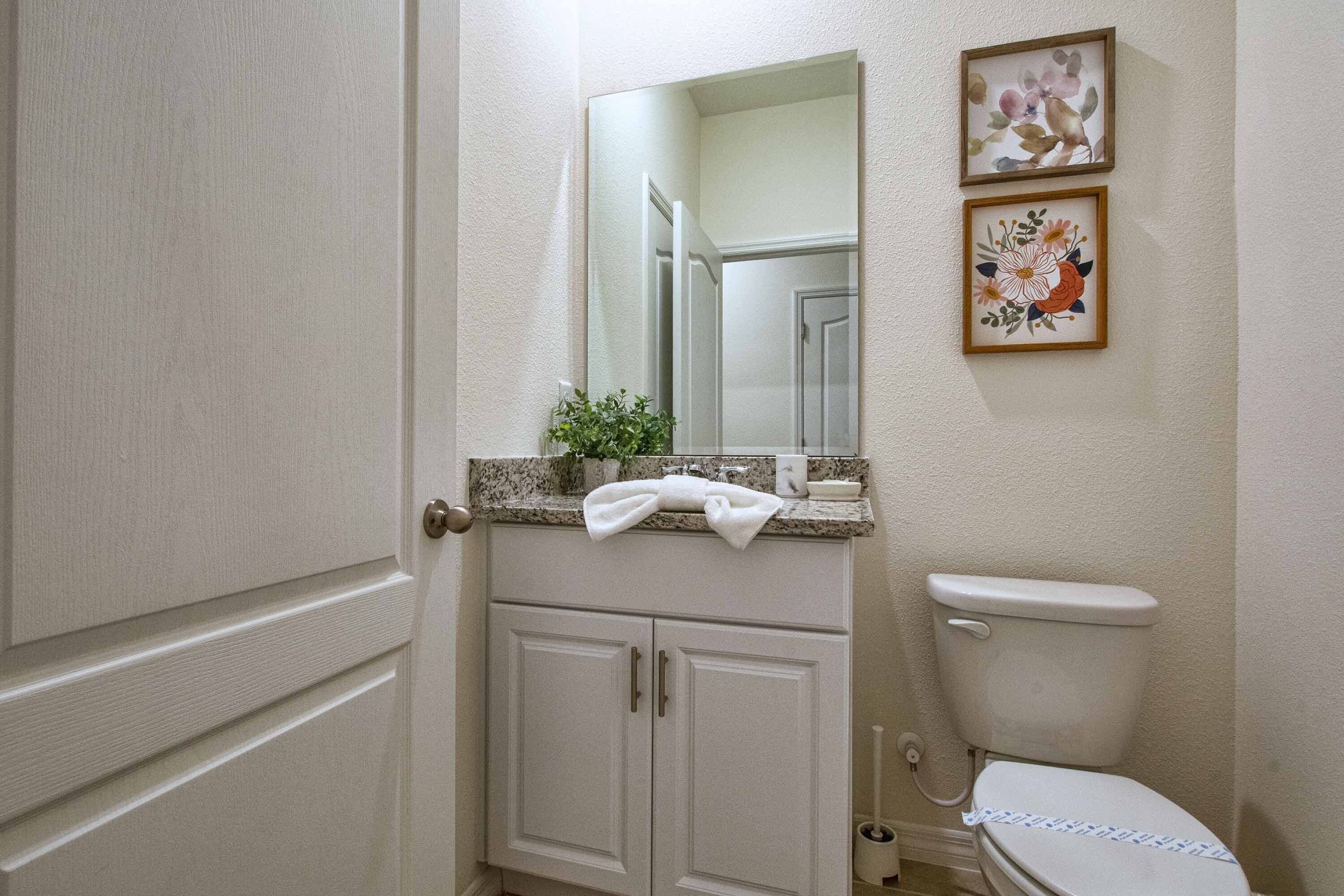 Une salle de bain comprenant des toilettes, un lavabo avec un miroir et deux tableaux représentant des motifs floraux, accrochés au mur.