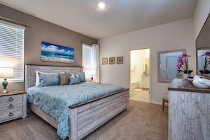 A bedroom with a bed, a dresser, a mirror, and a painting of the ocean.