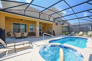 A pool area with lounge chairs, a hot tub, and a covered patio with outdoor furniture.