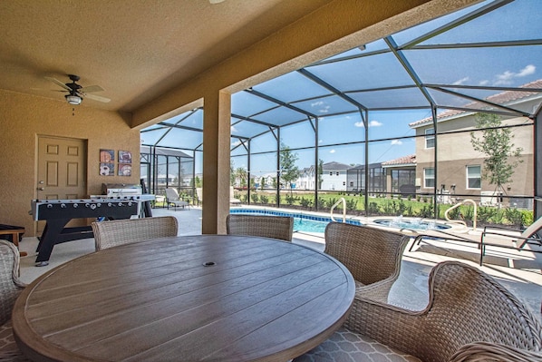 An outdoor patio with a pool, a foosball table, and wicker furniture.