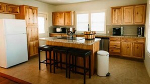 A kitchen with wooden cabinets, a white refrigerator, a granite countertop, and a trash can.