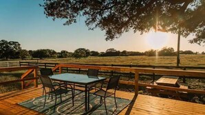 An outdoor wooden deck with a table and chairs, surrounded by a wooden fence, overlooking a grassy field.