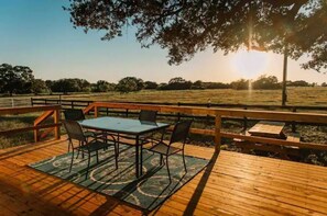 Enjoy a meal or a moment of peace on this outdoor deck with a glass table and four chairs, surrounded by a grassy field.
