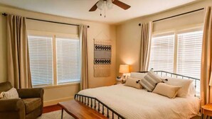 A bedroom with a bed, a bench, a chair, a ceiling fan, and a wall-mounted lamp.