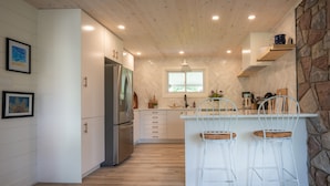 Una cocina moderna con armarios blancos, una isla integrada con taburetes de bar, una pared de acento de piedra y un ventanal que proporciona luz natural.