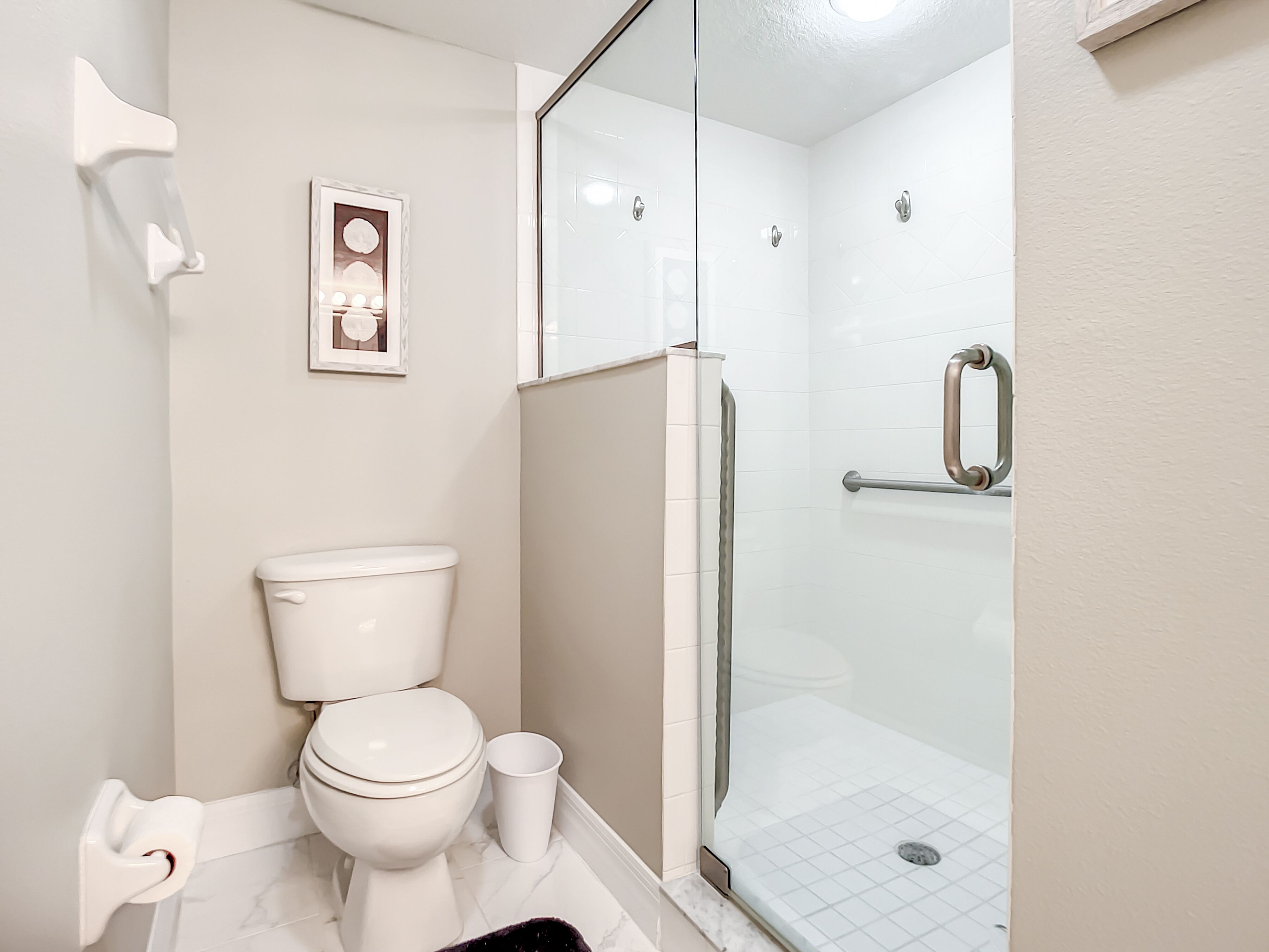 A modern bathroom with a toilet, a glass shower enclosure, and a handrail.