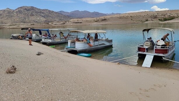 A calm lake with several boats docked at the shore, surrounded by a mountainous landscape. - Family Style Lake House (Meadview)