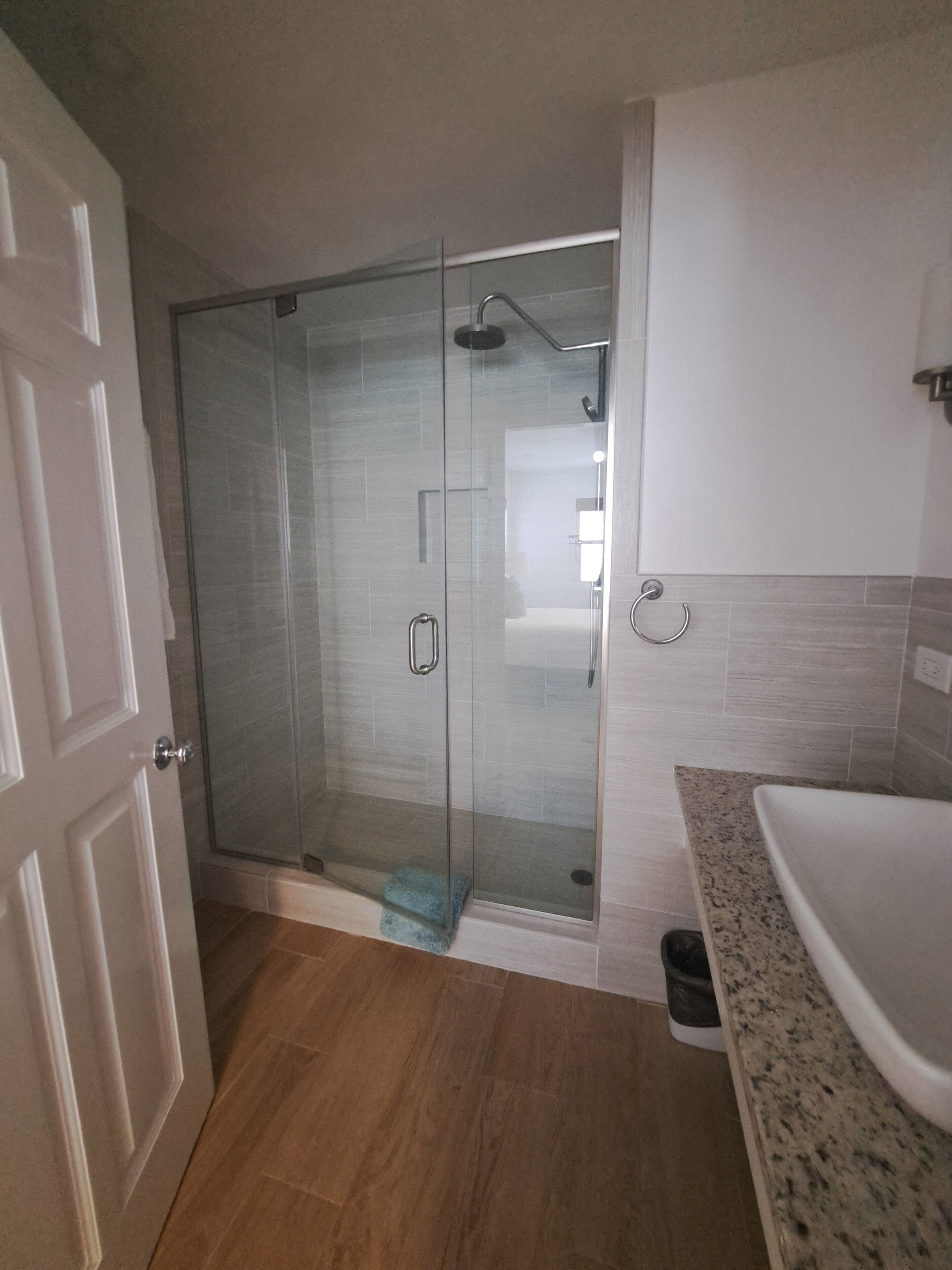 A bathroom with a glass-enclosed shower, a sink, and a door.