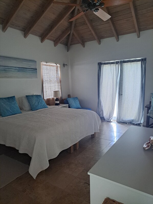 Un dormitorio con una cama grande, techo de madera, mesita de noche, lámpara y ventana con cortinas.