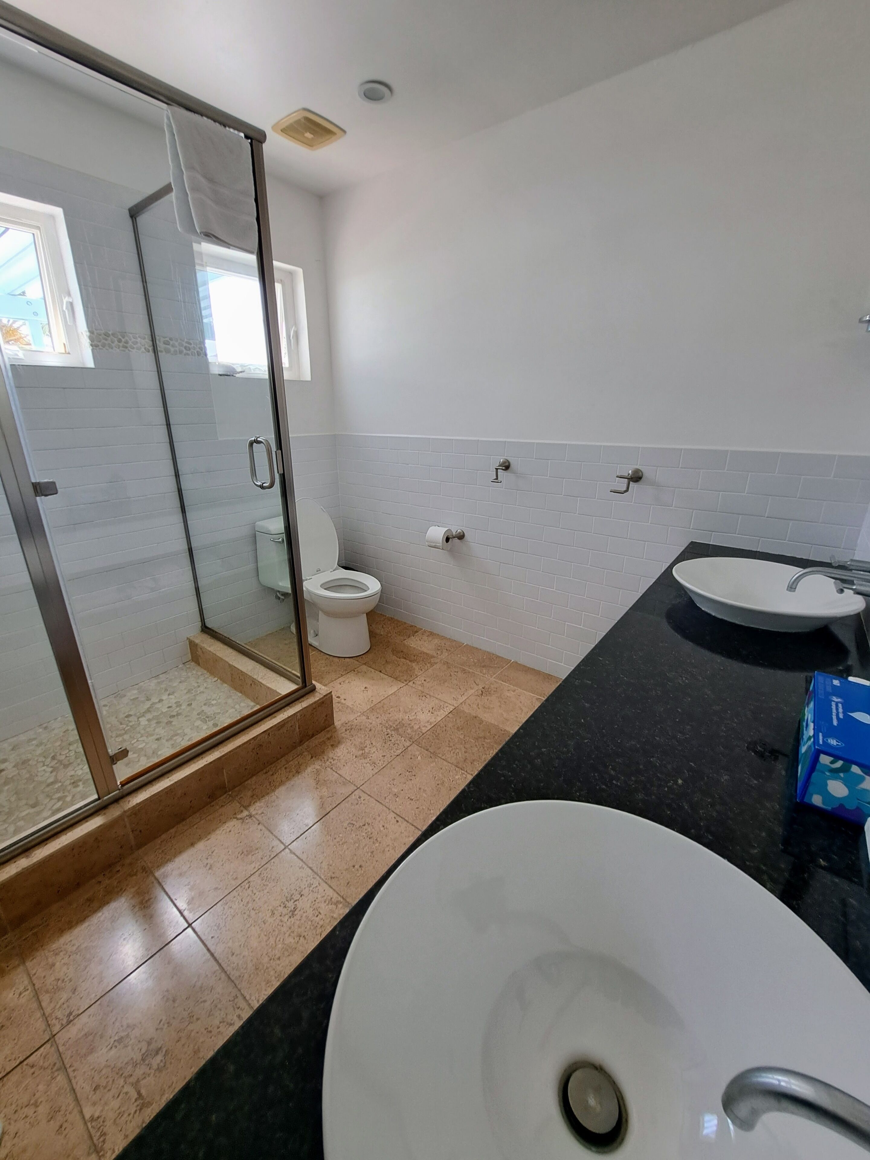 A bathroom with a glass shower enclosure, a toilet, and two sinks.