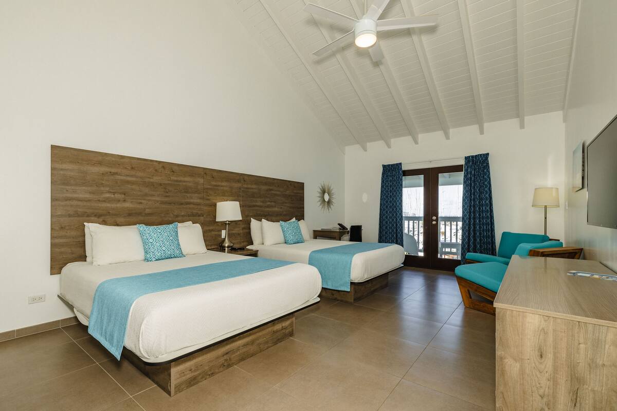 Une chambre d’hôtel avec deux lits, un ventilateur de plafond, une télévision et un balcon avec des rideaux.