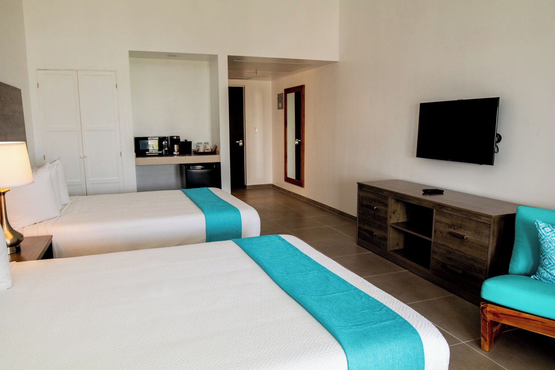 Ein Hotelzimmer mit zwei Betten, einem Fernseher, einem Schreibtisch mit Computer und einer Küchenzeile.