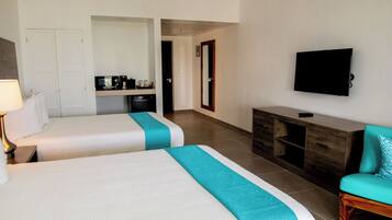Quarto de hotel com duas camas, televisão, escrivaninha com computador e cozinha compacta.