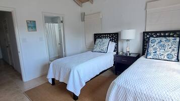 A bedroom with two beds, a ceiling fan, a wooden ceiling, and a view of the beach.