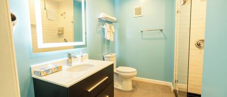 Une salle de bain avec un lavabo blanc, des meubles sombres, des toilettes blanches et une cabine de douche en verre.