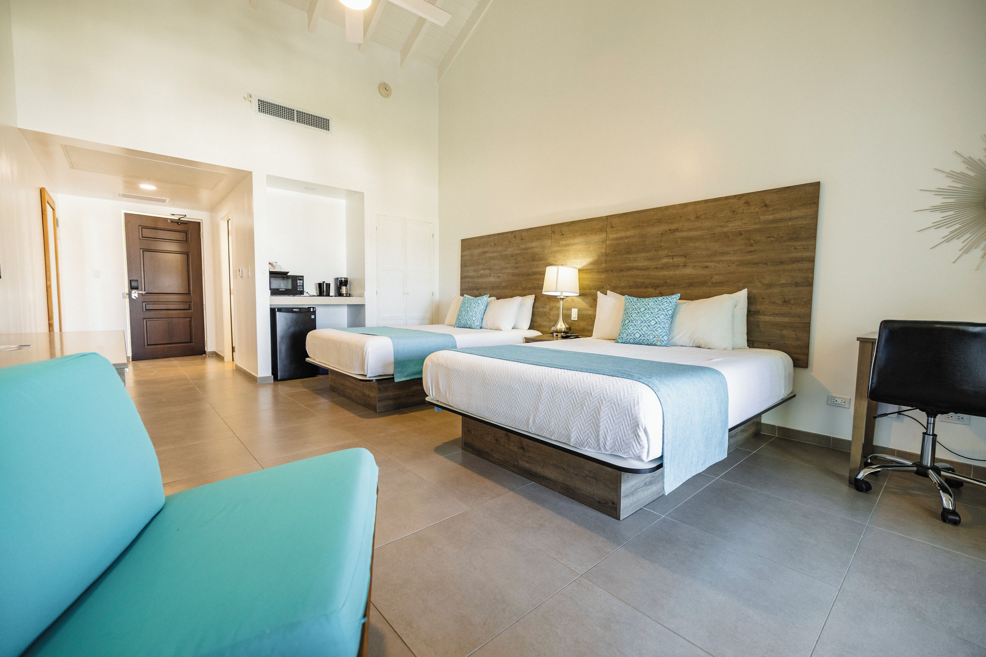 A hotel room with two beds, a kitchenette, a bathroom, and a seating area.